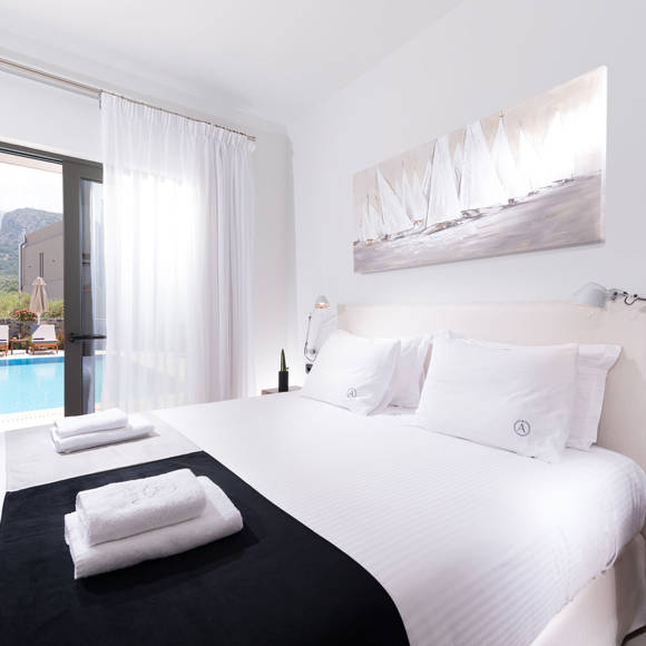 Grand villa bedroom with double bed, pool view through glass door and bright natural light at Avdou Collection Crete