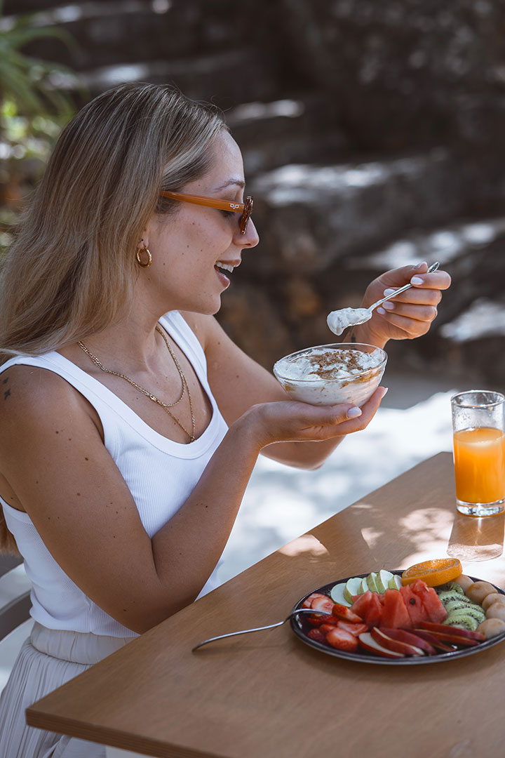 Guest enjoying breakfast outdoors with Greek yogurt, fresh juice and plate with fruit at Avdou Collection Crete
