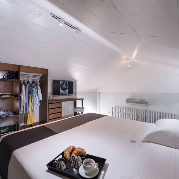 Loft bedroom with slanted ceiling, large bed, open wardrobe and TV at Avdou Collection Crete