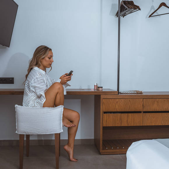 Guest sitting at a wooden dressing table in a modern villa bedroom at Avdou Collection Crete