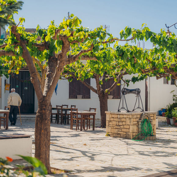 Avdou village in Crete in a sunny day with trees, outdoor tables and a stone well 