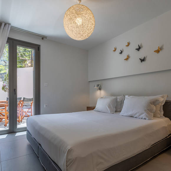 Suite's modern bedroom with double bed and balcony door, minimalist decor and bedside table at Avdou Collection