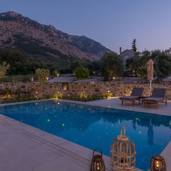 Grand villa pool with lanterns, sunbeds and evening mountain views in serene atmosphere at Avdou Collection
