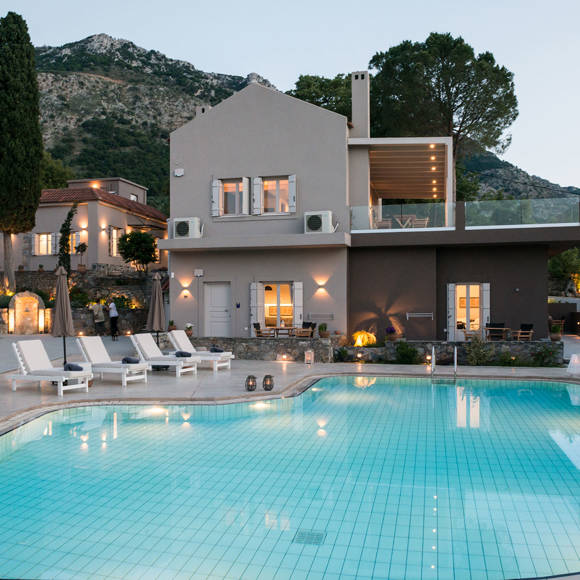 Evening view of the illuminated swimming pool with sun loungers and mountain backdrop at Avdou Collection Crete