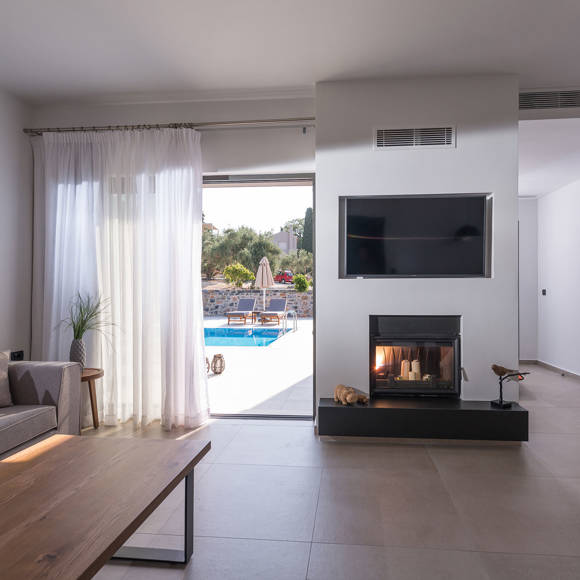 Grand villa living room with sofa, fireplace, wall mounted TV and direct access to the pool at Avdou Collection Crete